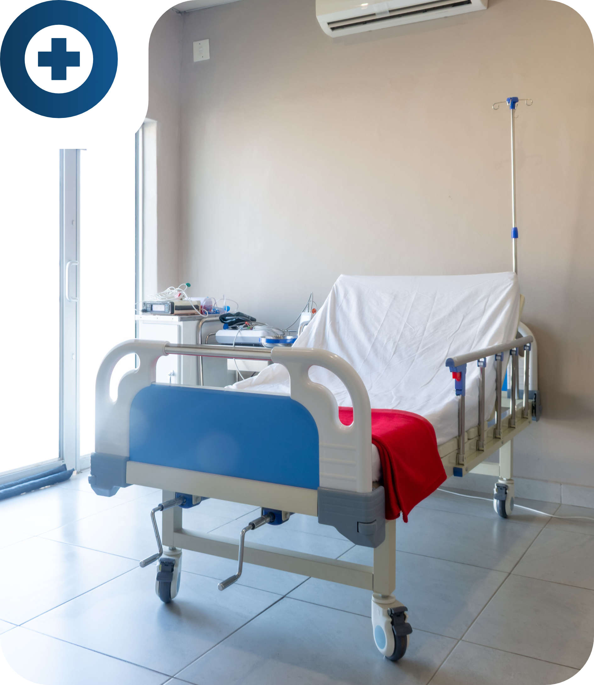 Empty hospital bed with a white sheet and red blanket in a clean hospital room with medical equipment and IV stand nearby.