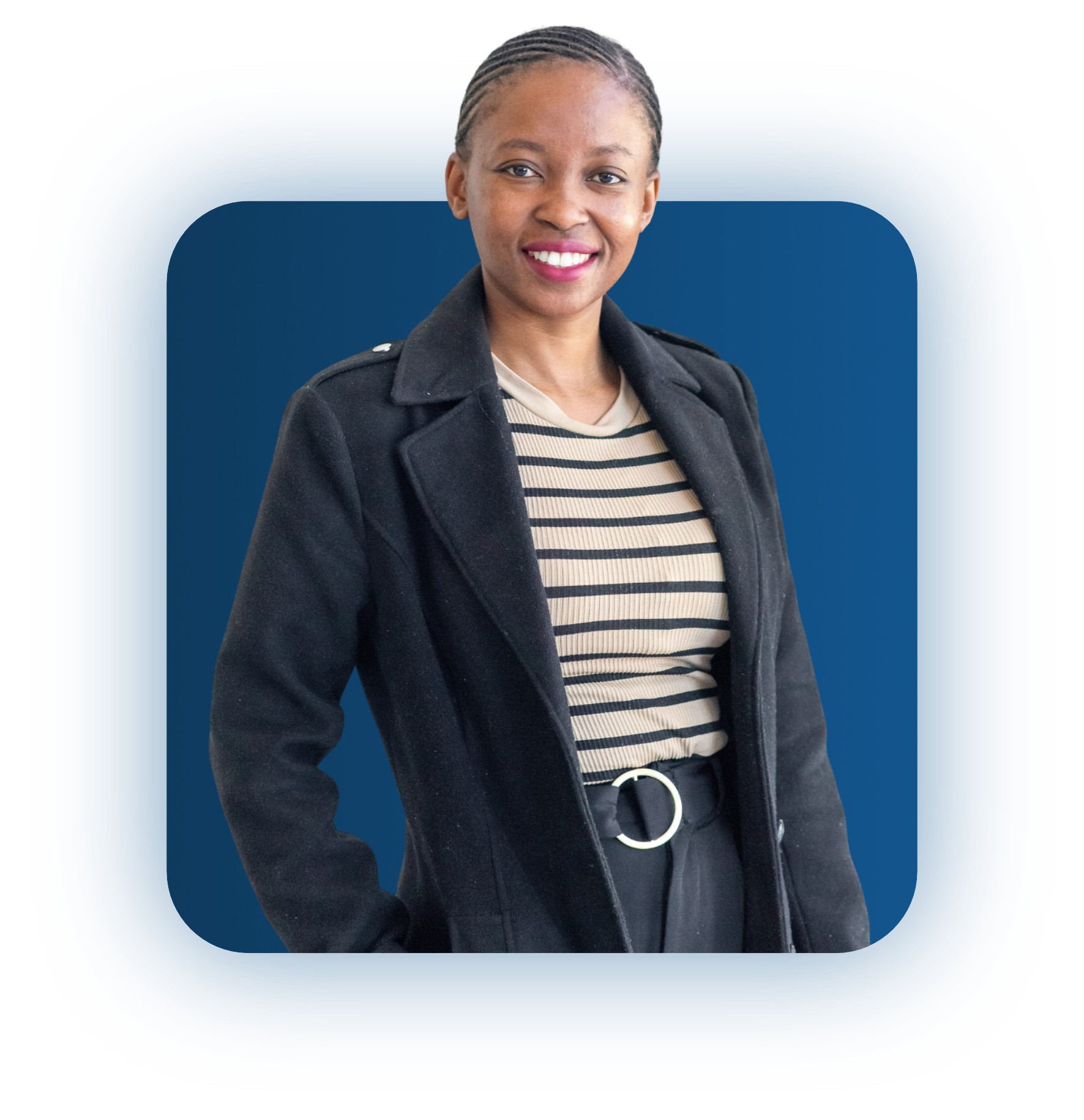 Smiling woman with braided hair wearing a black coat over a beige and black striped top and black pants with a belt standing against a blue background.