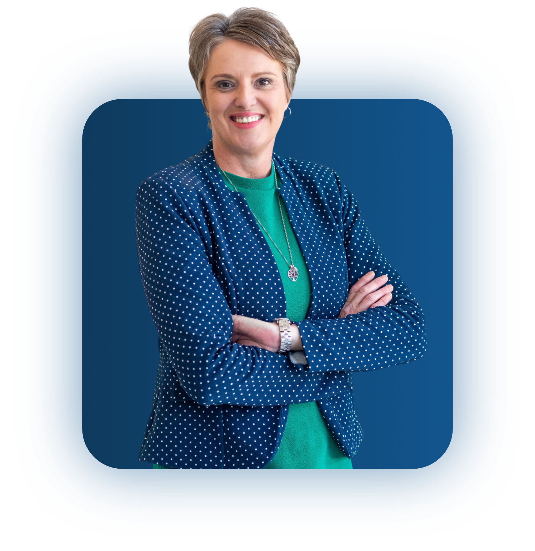 Smiling woman with short hair wearing a blue polka dot blazer and green top, arms crossed.