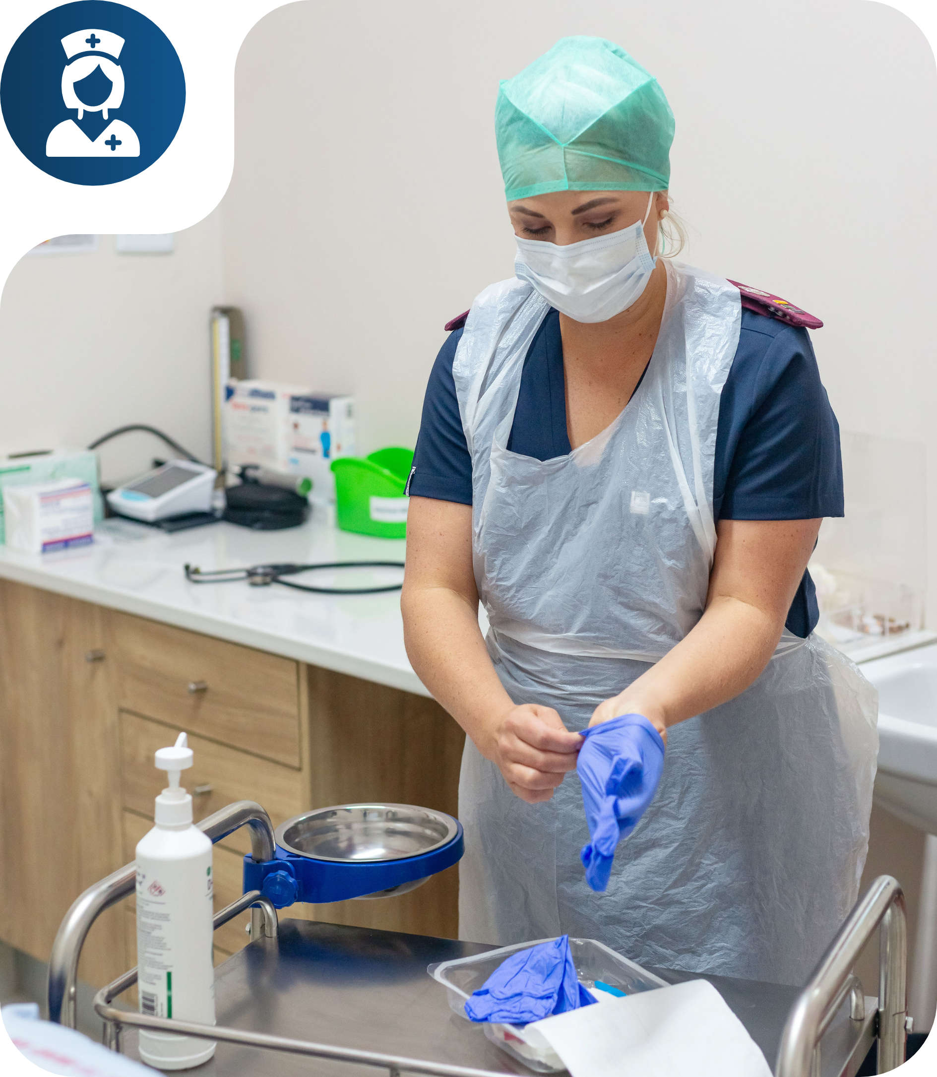Healthcare worker wearing a surgical mask and cap putting on blue gloves in a medical room.